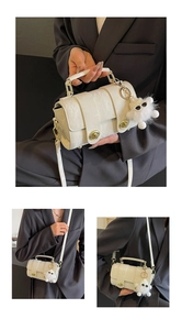Detail view of cream textured barrel bag featuring gold hardware and a cute plush charm