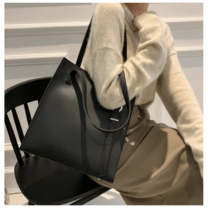 Macro shot of minimalist black leather tote bag featuring a decorative silver metal buckle