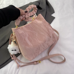 Sac seau plissé rose avec poignée tressée et charm en peluche sur fond gris