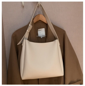 Detail of cream soft leather tote bag hanging on wooden hanger with brown coat background