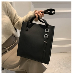 Detail of a black matte tote bag featuring dual silver rings and minimalist leather straps