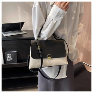 Detail of a contrast color leather bag with a golden round buckle on a crossbody strap