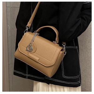 Detail of tan pebble leather handbag featuring a silver charm and adjustable strap