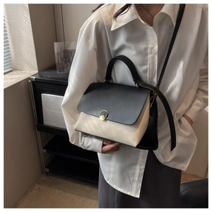 Detail of contrast color leather handbag featuring a gold round clasp and top handle