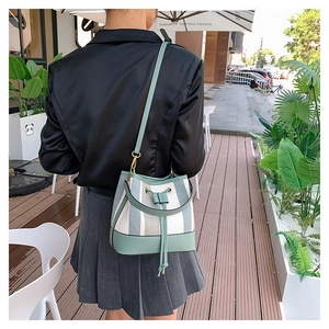 Borsa a secchiello a righe con finiture in pelle verde indossata come borsa a spalla
