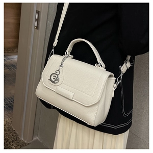 Detail view of cream white lychee leather handbag with a silver swan pendant on a model