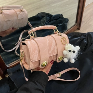 Pink textured Boston bag with gold hardware and white plush charm on mirror surface
