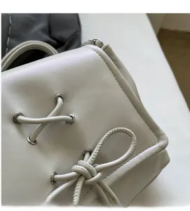 Dettaglio ravvicinato della borsa in pelle beige con fiocco decorativo e occhielli in argento