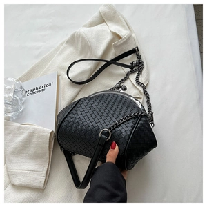 Detail of a black woven shell crossbody bag with retro metal clasp and chain strap