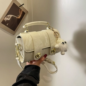 Cream white cylindrical handbag with golden twist lock and plush charm on beige background