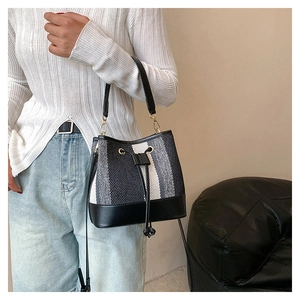 Dettaglio di una borsa a secchiello intrecciata a righe nere, grigie e bianche con coulisse
