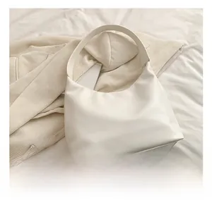 Detailed view of the white minimalist hobo bag placed on soft white fabric background