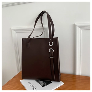 Detail of dark brown leather tote bag with silver metal rings on a wooden table