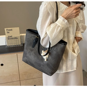 Detail of dark gray tote bag with leather straps and a cute plush monster charm