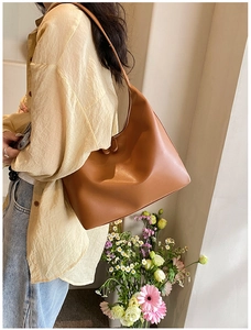 Detailed side view of a large caramel leather hobo bag worn by a model in a floral setting