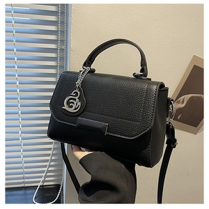 Close-up of black litchi grain leather handbag featuring a silver swan pendant detail