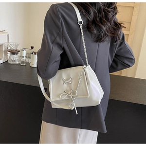Dettaglio borsa crema con fiocco e catena d'argento su un blazer nero chic