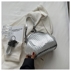 Close-up of a silver woven shell bag with metal clasp and chain on a white fabric background