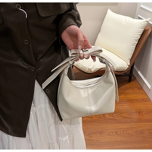 Detail of a creamy white glossy patent leather crescent bag with a decorative bow handle