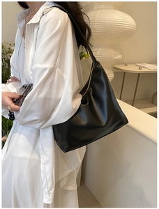 Close-up of a black matte leather hobo shoulder bag with a gold zipper on a model