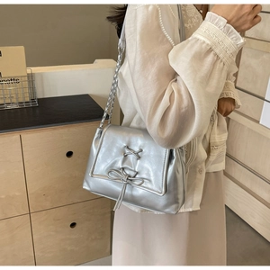 Dettaglio della borsa argento metallizzato con fiocco e catena indossata dalla modella