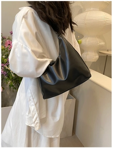 Detail of a black half-moon hobo bag with matte leather texture worn on the shoulder