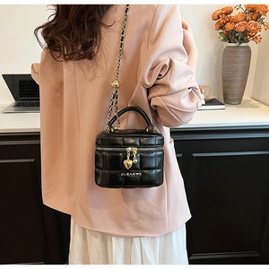 Détail d'un sac matelassé noir à chaîne avec breloque cœur dorée et logo