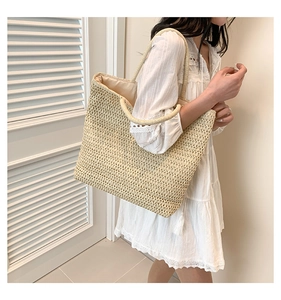Détail de la texture d'un sac cabas en paille tressée porté avec une robe blanche