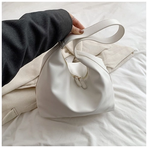 Minimalist white faux leather hobo bag with gold zipper held by a model in a lifestyle setting