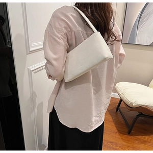 Side view of a minimalist white rectangular underarm bag worn by a model in a stylish room