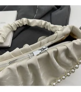 Detail shot of a smooth silver zipper and textured pleated beige faux leather shoulder bag