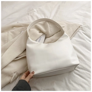 Minimalist white leather underarm bag with sleek curved silhouette on a beige blazer