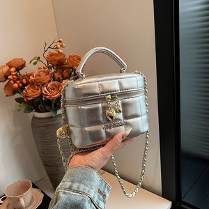 Sac seau matelassé argenté avec bandoulière chaîne et breloque cœur à la main