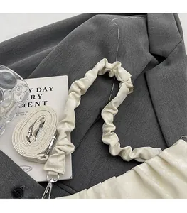 Detail of cream pleated shoulder strap and silver buckle on a stylish crossbody bag