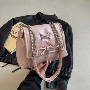 Elegante borsa a tracolla rosa in pelle con fiocco e catena su sfondo di giacca nera