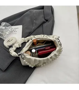Detail of cream pleated cloud bag with pearl chain and adjustable strap on a grey suit