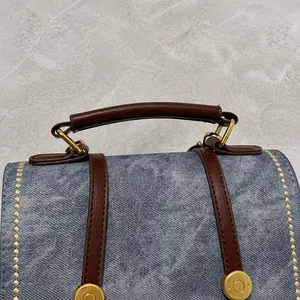 Close-up of blue denim handbag with brown leather handles and gold metal hooks