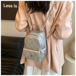 Detail of silver quilted mini backpack with metallic chain straps on a model's back