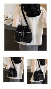 Detail of a chic black bucket bag featuring silver chains and zipper on textured fabric