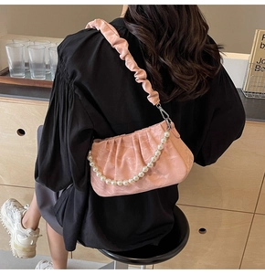 Détail du sac plissé rose avec chaîne en perles porté par un mannequin en noir