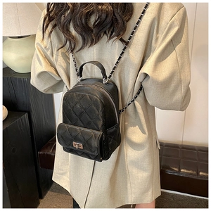 Detail of a mini quilted backpack with chain straps and turn-lock on a model