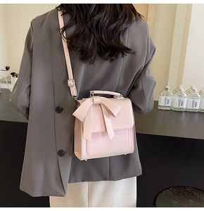 Detail showing a pink crossbody bag with a bow decoration on a grey blazer outfit