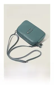 Detail of teal pebble leather crossbody bag with silver U-shaped metal buckle closure