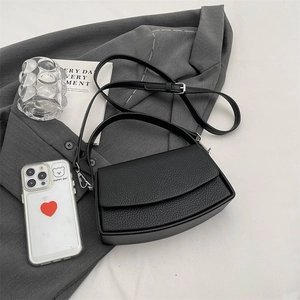 Minimalist black pebble leather shoulder bag on a grey blazer in a modern setting