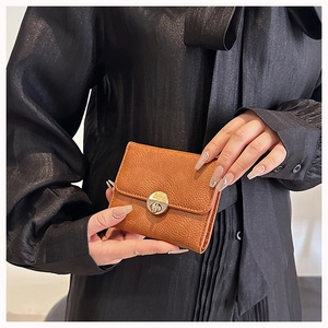 Close-up of caramel pebble leather wallet with round gold clasp held by elegant hands