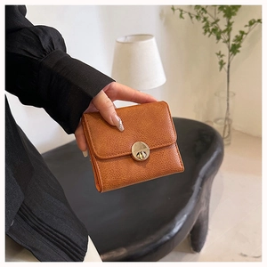 Brown lychee leather wallet with a golden twist lock held in a lifestyle setting