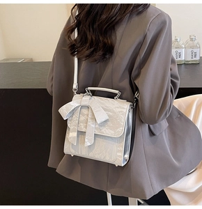 Silver textured handbag featuring a large bow detail and metallic handle on model side view
