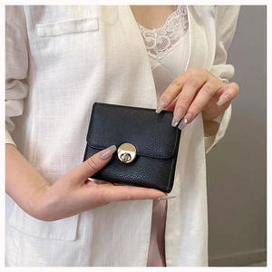 Detail of black pebbled leather wallet featuring a round golden metallic twist-lock
