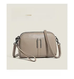 Detail of khaki pebbled leather crossbody bag with U-shaped metal accent and dual zippers