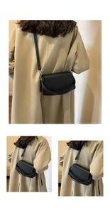Detail of black pebbled leather crossbody bag with silver hardware on a beige trench coat